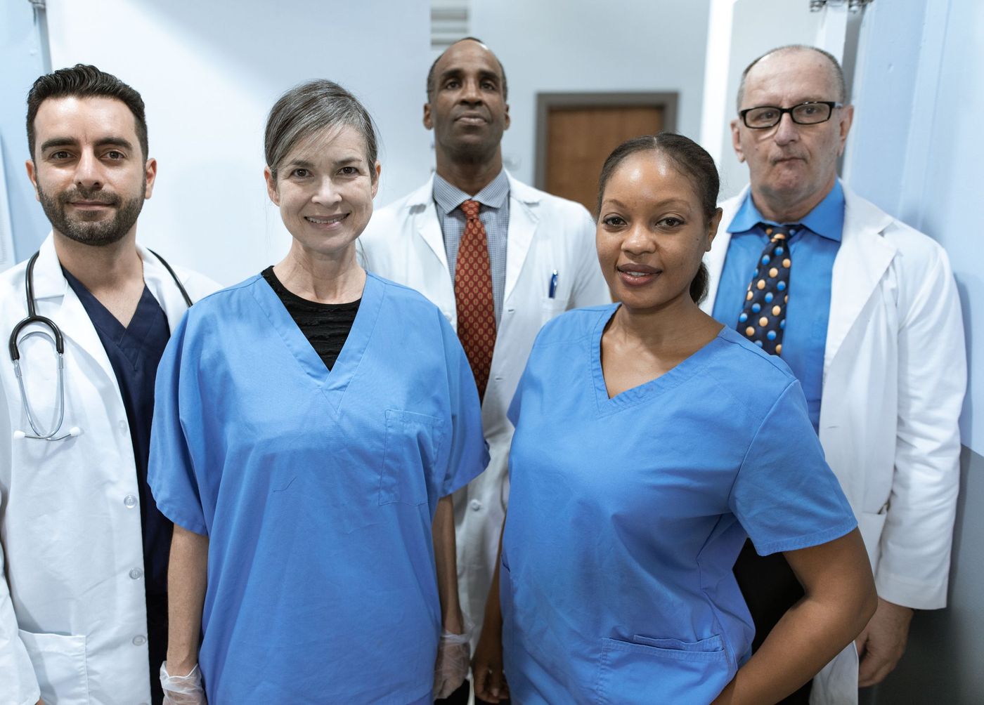 A diverse clinical team of nurses in blue scrubs and physicians in white coats standing together and smiling