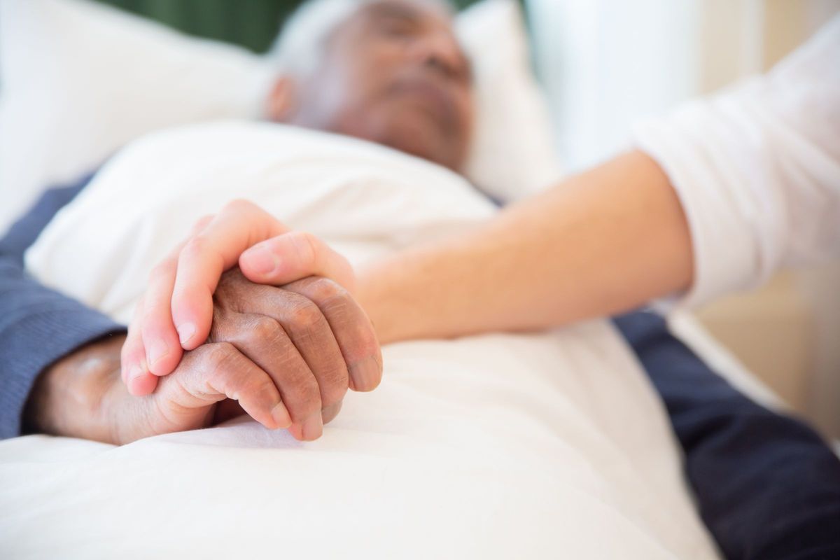 Close-up of a caregiver gently holding the hand of an older man resting in bed